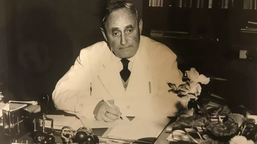 Svartvitt foto på en äldre man som sitter vid ett skrivbord.